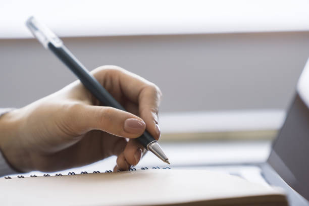 istock The image focuses on a woman's hand scribbling in a notepad on a stylish laptop, set against a blurry scene 1499801458