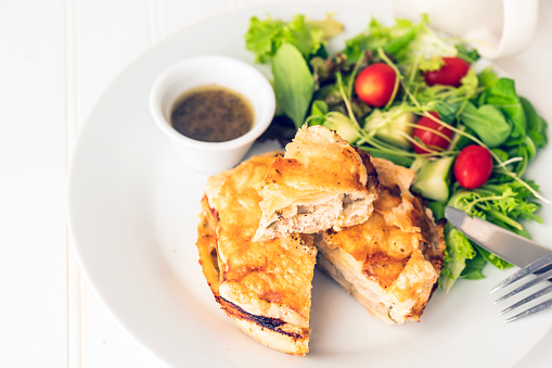 A still life of a savory chicken pie with short crust pastry and a puff pastry top. Shown with a side salad.