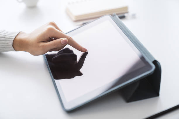 istock Woman's hand operating a modern tablet device placed on a desk, surrounded by the blurry contours of a well-lit office space 1499801570