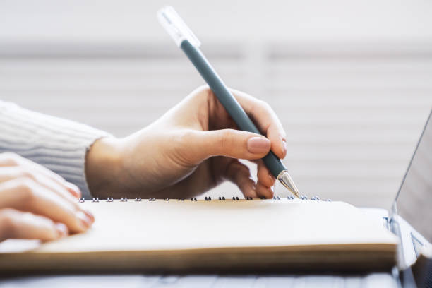 istock A woman's hand inscribing in a notepad, captured closely, with a vague background 1499801602