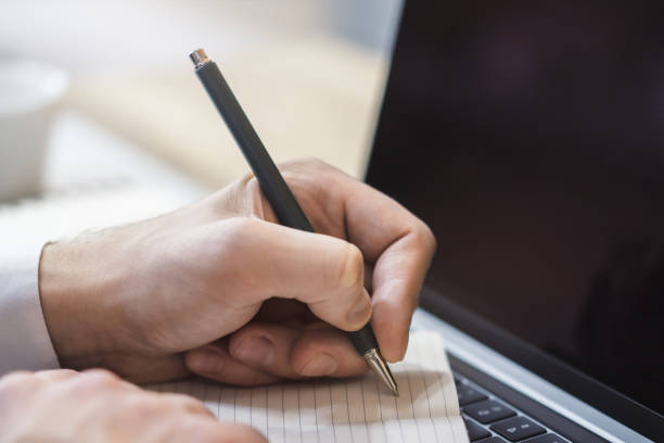 istock The image focuses on a man's hand scribbling in a notepad on a stylish laptop, set against a blurry scene 1499801677
