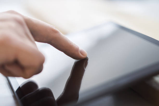 istock Man's finger operating a modern tablet device placed on a desk, within the blurry contours of a well-lit office space 1499801682