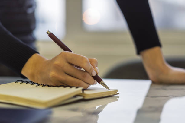 istock A woman's hand inscribing in a notepad, captured closely, with a vague background 1499801796