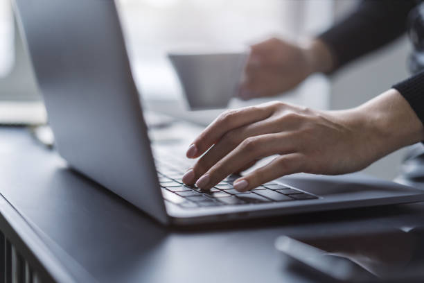 istock Female hands in sharp focus typing on a modern laptop keyboard, office environment in soft blur behind 1499801904