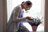 Woman contemplates lavender bouquet, sitting on window frame.