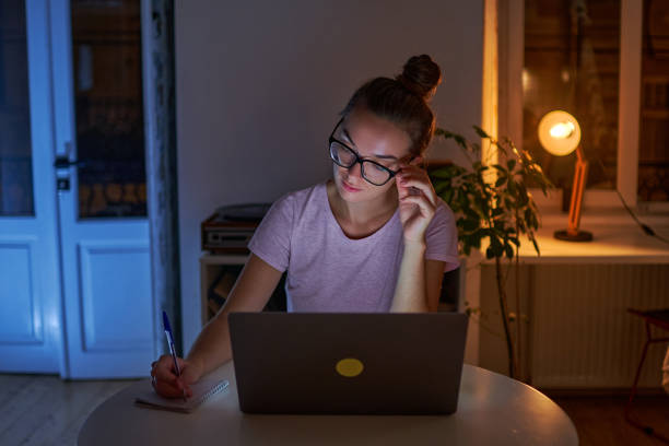 istock Serious woman workaholic in glasses makes a note in a notebook during late work at a laptop at home 1499804835