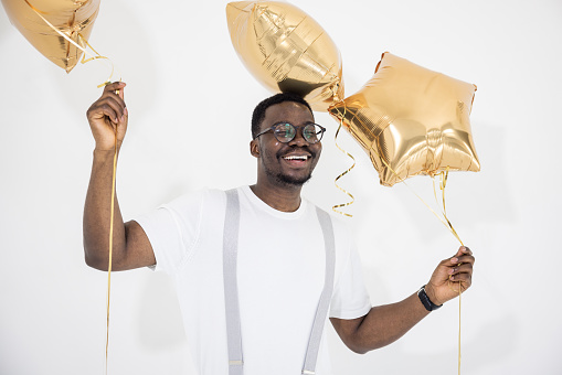 Portrait of a happy guy holding balloons and dancing under glittering confetti.