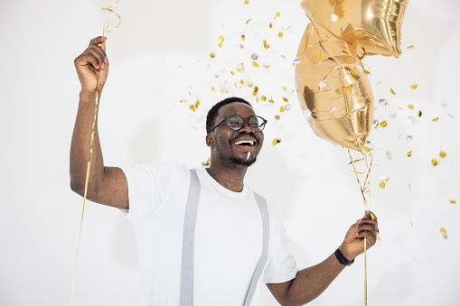 Portrait of a happy guy holding balloons and dancing under glittering confetti.