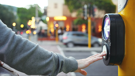 Close-up shot of an unrecognisable pedestrian hand pressing the walk button to safely cross the street at a crosswalk