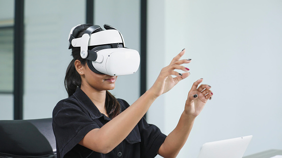 Young woman wearing VR virtual reality glasses and raised hands touches the air. Simulation and metaverse concept