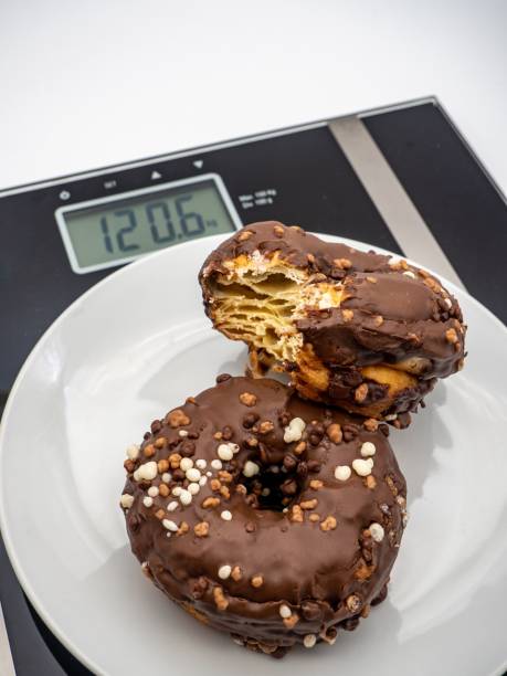 istock Closeup of a white plate with two delectable chocolate donuts on a weight scale 1499816534