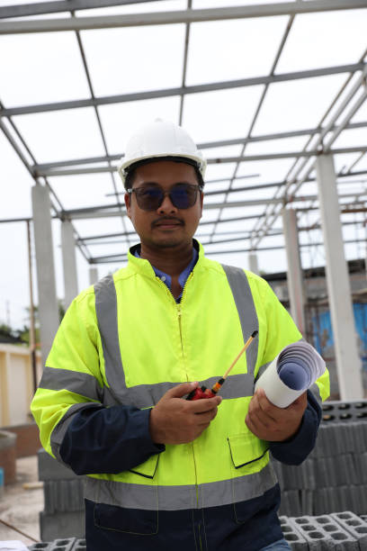 istock Construction engineer with green reflective safety jacket hold laptop working in  construction site with walkie talkie communication with team. Blueprint document , drawing pattern 1499816706