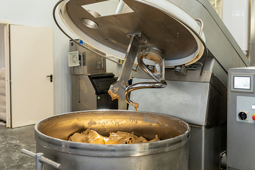 Industrial machine for mixing dough in bakery. Upper part of mixer is raised, finished dough is in bowl. One of stages of bread production. Production of bread, rolls, confectionery