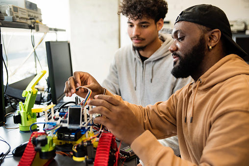 Diverse team of college students in robotics classroom. They are working on the small electronic cars they builded. STEM topic Horizontal waist up indoors shoot with copy space. This was taken in Quebec, Canada.