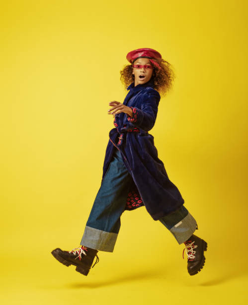 Little girl looking at camera while jumping in front of yellow background.