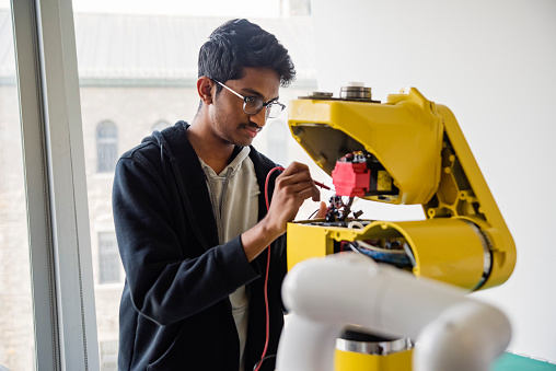 College student in robotics classroom. Young man of Indian ethnicity. He is working on an electronic machine. Horizontal waist up indoors shoot with copy space. STEM topic. This was taken in Quebec, Canada.
