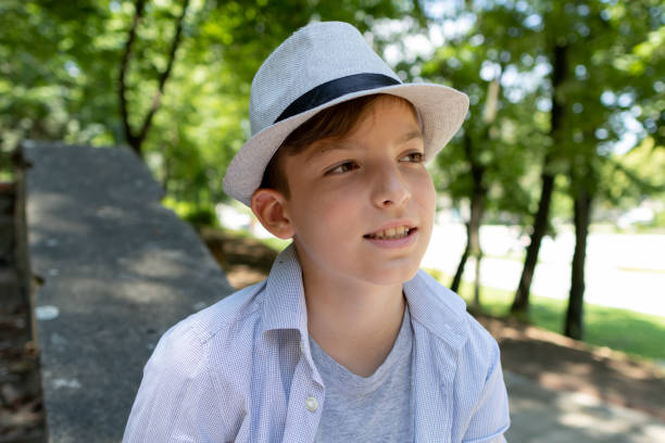 Boy with hat sitting on the park bench and drawing in the park.