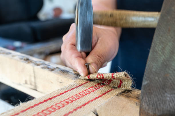 Upholsterer fixes a new strap with hammer and nails to restore an old chair in his workshop, traditional craftsmanship copy space, motion blur, selected focus stock photo