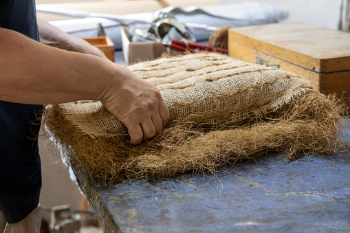 Upholstery craftsman shapes a pack filled with plant fibers like coir or palm fiber for a seat or sofa, traditional craft skill to create or repair furniture with natural material, copy space, selected focus