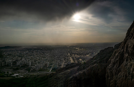 The city of Tehran is viewed from the mountains with the sun peeking from underneath the clouds