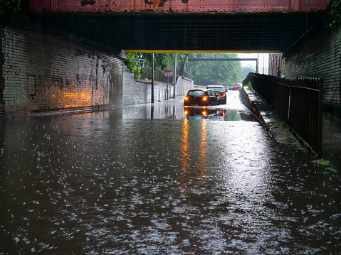 Two cars stranded in flood water under low bridge in Salford city street flashing emergency lights.