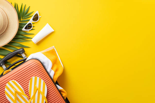 istock Sun-soaked dreams. Top view setup displaying a suitcase, beach essentials, glasses, sunhat, sunscreen, flip-flops, towel, palm leaf on vibrant yellow backdrop. Empty space provided for text or adverts 1499834957