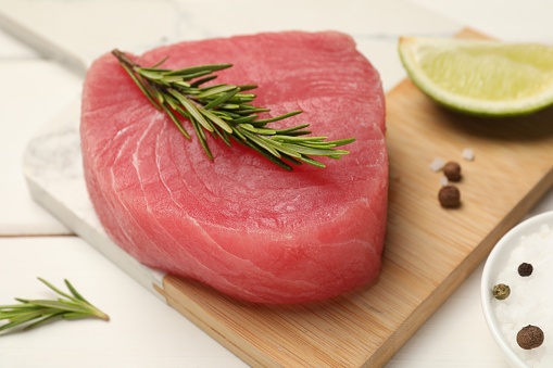 Raw tuna fillet with rosemary and spices on white table, closeup