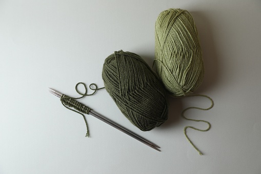 Soft green yarns, knitting and metal needles on light background, flat lay