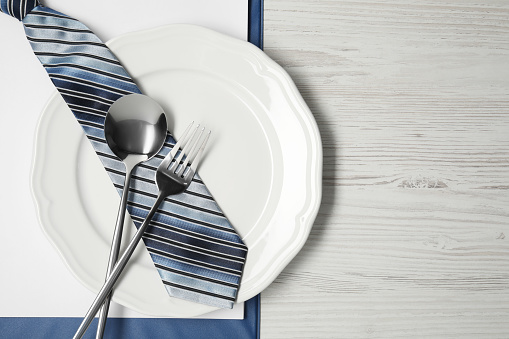 Plate with cutlery, tie and clipboard on wooden table, top view and space for text. Business lunch concept