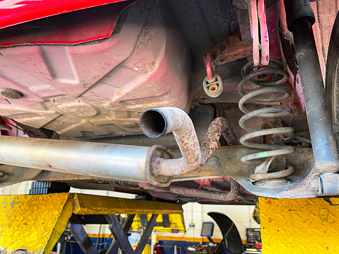 Stock photo showing close-up view of broken down red car in mechanic's garage supported on pantograph scissor car lift in order to access the vehicle's undercarriage for repairs.