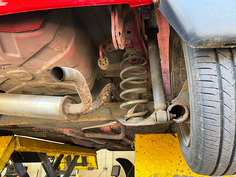 Stock photo showing close-up view of broken down red car in mechanic's garage supported on pantograph scissor car lift in order to access the vehicle's undercarriage for repairs.