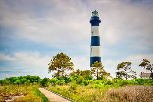 A coastal lighthouse landscape with a wooden boardwalk over marshland in colorful High Dynamic Range (HDR).