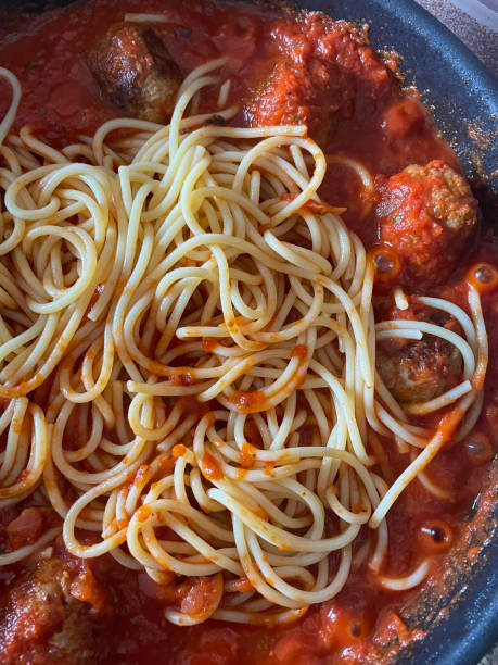 Close-up image of cooked meatballs added to frying pan with freshly cooked spaghetti pasta and tomato ragu sauce, homemade pork balls, elevated view