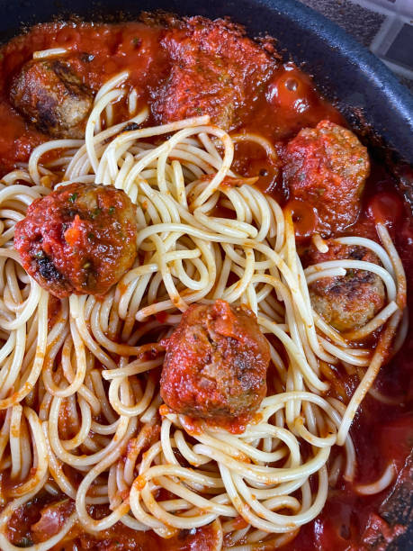 Close-up image of cooked meatballs added to frying pan with freshly cooked spaghetti pasta and tomato ragu sauce, homemade pork balls, elevated view