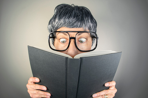 A fisheye mage of a nerdy woman with gray hair and glasses getting into a book.
