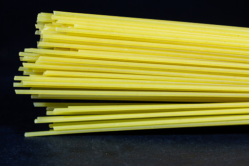 Picture of spaghetti, isolated on a black background. Spaghetti is a long, thin, solid, cylindrical pasta. It is a staple food of traditional Italian cuisine. Like other pasta, spaghetti is made of milled wheat, water, and sometimes enriched with vitamins and minerals. Italian spaghetti is typically made from durum-wheat semolina.