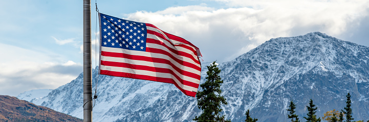 Panoramic mountain setting behind an American, United States flag. Stars and stripes in Alaska.
