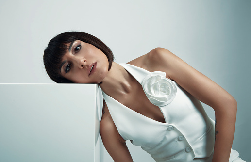 Portrait of woman with short, blunt hair leaning her head on white box and looking at camera.