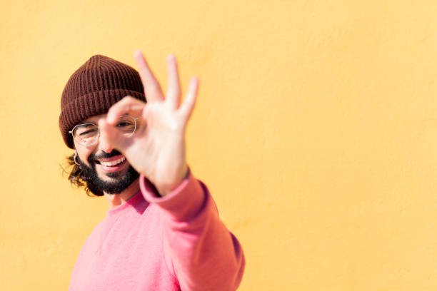 man doing ok sign with hand in a yellow background