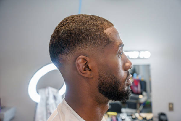 jovem afro-americano recebendo corte de cabelo desbotado de barbeiro mexicano em uma barbearia à moda antiga com cortadores elétricos - fade in - fotografias e filmes do acervo