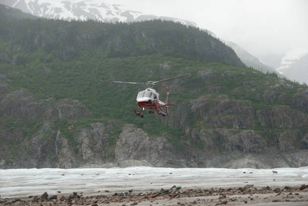 Helicopter lands on a glacier carrying lose rocks and ice between mountains