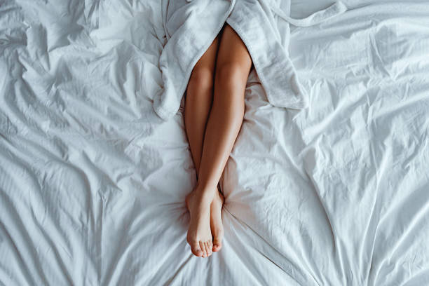 istock Lazy woman wearing bathrobe with slim smooth long beutiful legs lying on white bed and relaxing at cozy comfort bedroom at hotel room. Easy lifestyle 1499876074