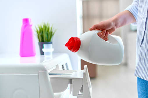 Female housewife pouring fabric softener gel into a modern washing laundry machine