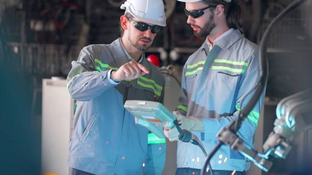 istock Engineer cooperation male technician uses control panel to control the operation of the robot arm system welding work piece and control quality operate process work heavy industry. Smart industry robot arms for production technology in factory. 1499880278