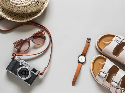 Women's accessories - comfortable sandals, straw hats, retro camera, sunglasses, wristwatch on a light gray background, top view