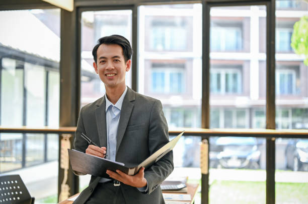 istock A smiling Asian businessman holding a business document folder while standing in his office. 1499893949