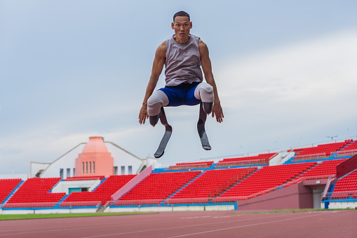 Victorious Asian speed runner, sporting two prosthetic running blades, performs a celebratory high jump after a successful speed running practice at the stadium