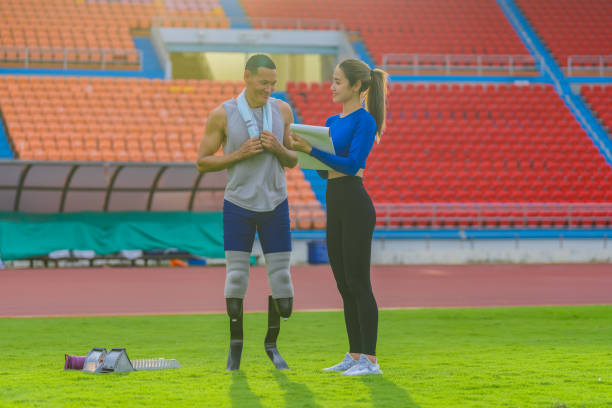 athlète masculin avec des lames prothétiques, aux côtés d’un entraîneur féminin, décrivant l’entraînement de course de vitesse de la journée au stade - track and field 30s adult athlete photos et images de collection