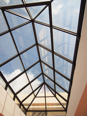 Glass roof of a greenhouse, barn or other agricultural building is made of transparent polycarbonate and wooden boards, sky clouds bottom view