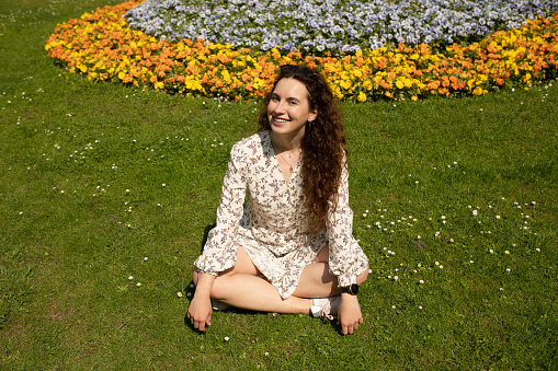Young woman outdoor sitting on grass, smiling.